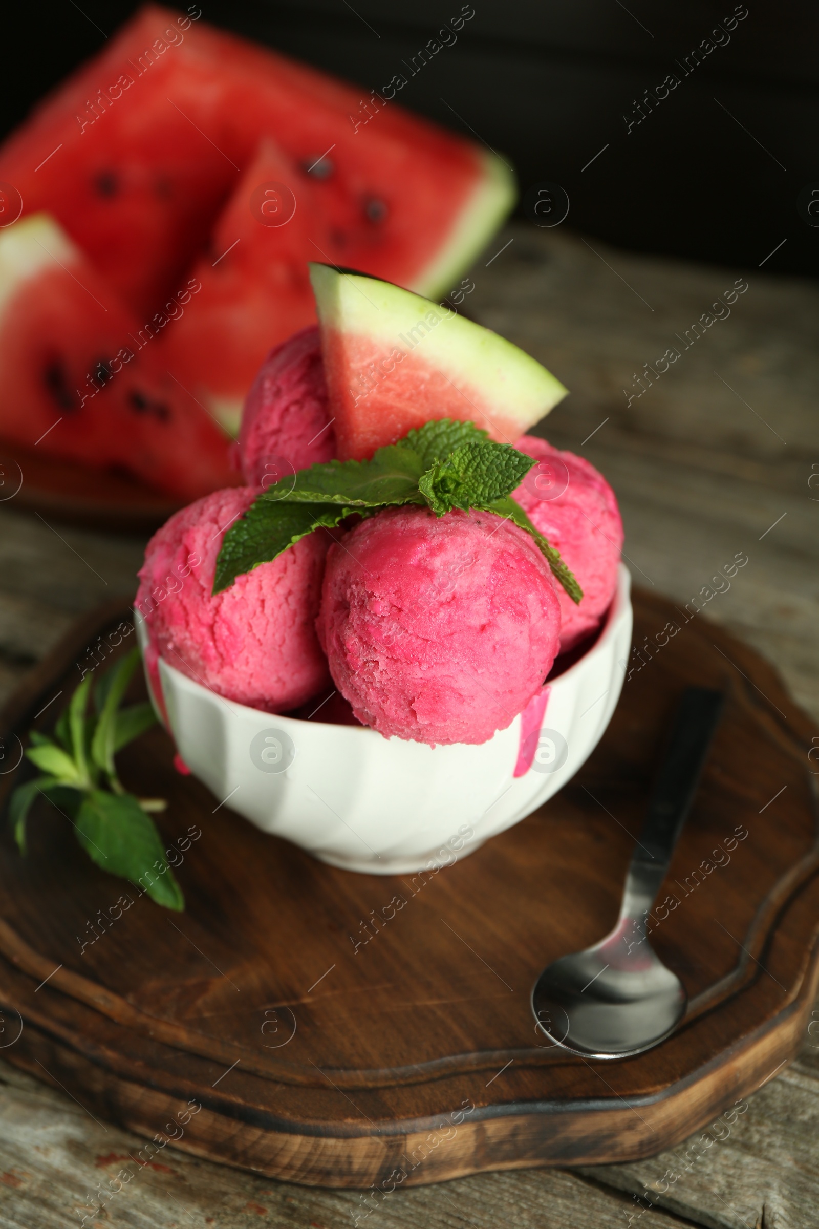 Photo of Scoops of tasty watermelon sorbet in bowl, fresh fruit, mint and spoon on wooden table