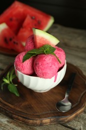 Photo of Scoops of tasty watermelon sorbet in bowl, fresh fruit, mint and spoon on wooden table