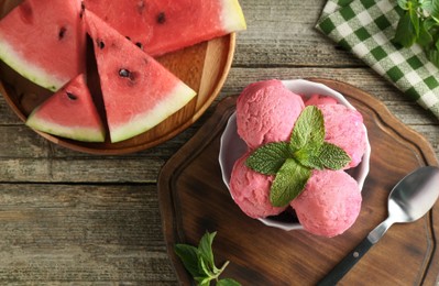 Photo of Scoops of tasty watermelon sorbet in bowl, fresh fruit, mint and spoon on wooden table, top view