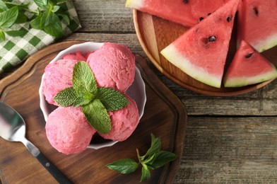 Photo of Scoops of tasty watermelon sorbet in bowl, fresh fruit, mint and spoon on wooden table, top view