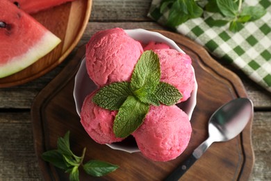 Photo of Scoops of tasty watermelon sorbet in bowl, fresh fruit, mint and spoon on wooden table, top view