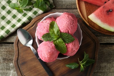 Scoops of tasty watermelon sorbet in bowl, fresh fruit, mint and spoon on wooden table, top view