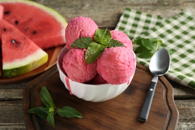 Photo of Scoops of tasty watermelon sorbet in bowl, fresh fruit, mint and spoon on wooden table