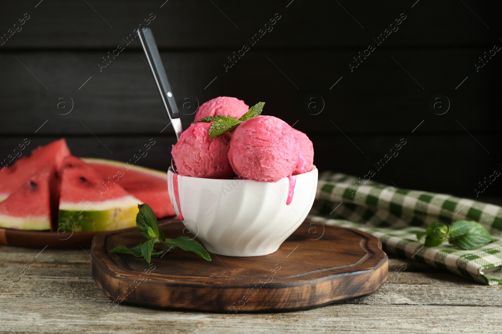 Photo of Scoops of tasty watermelon sorbet in bowl, fresh fruit, mint and spoon on wooden table