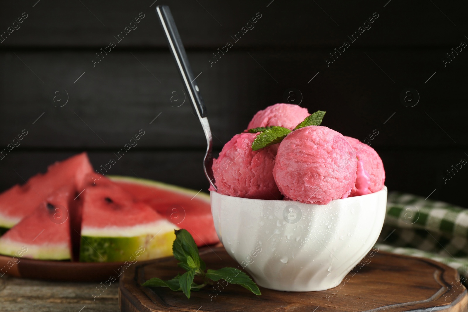 Photo of Scoops of tasty watermelon sorbet in bowl, fresh fruit, mint and spoon on wooden table