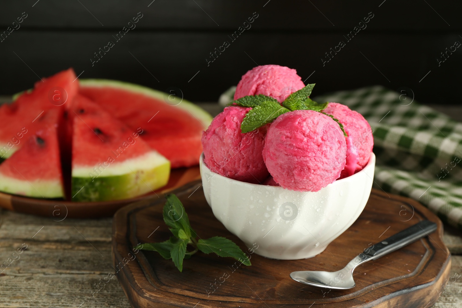 Photo of Scoops of tasty watermelon sorbet in bowl, fresh fruit, mint and spoon on wooden table