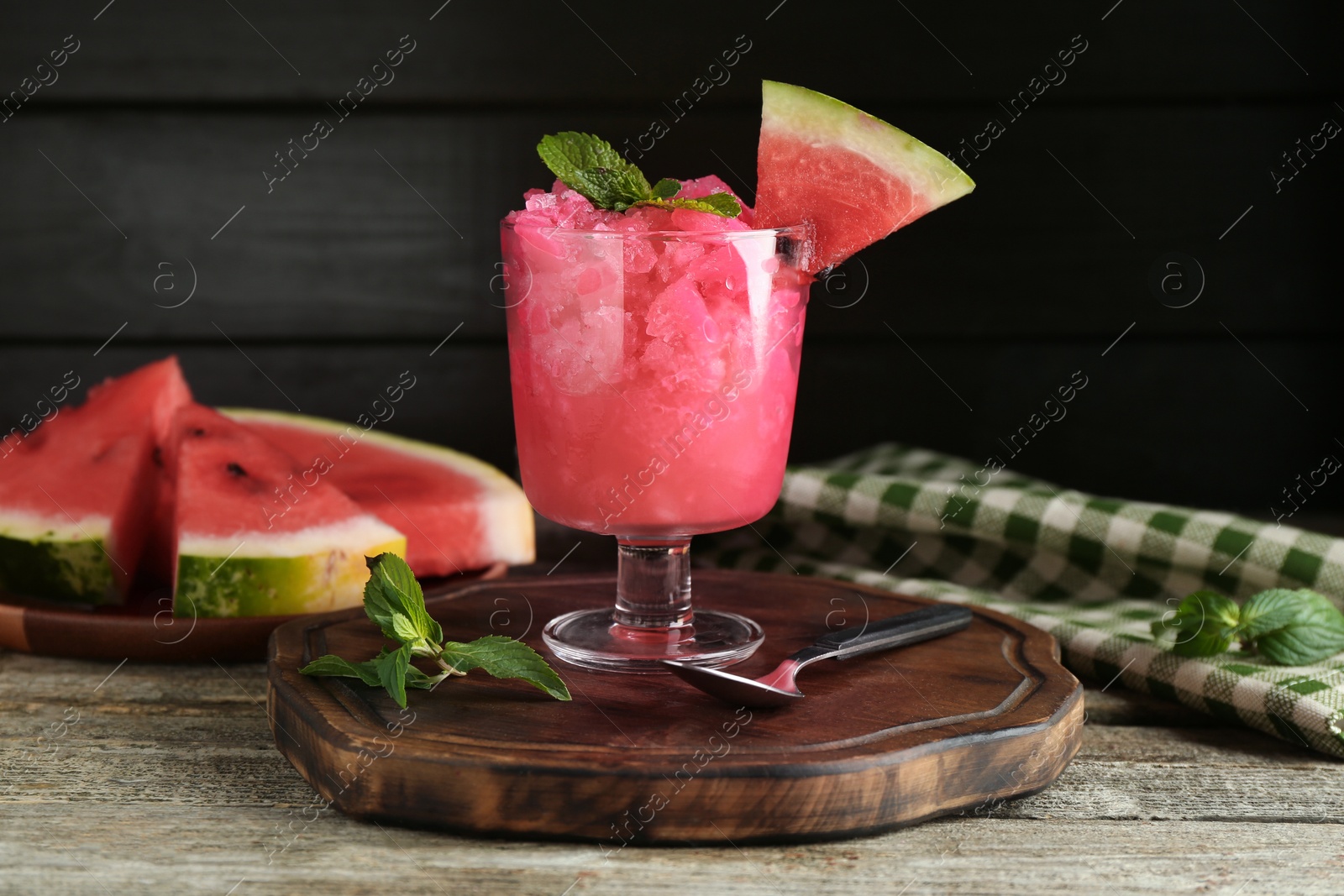 Photo of Tasty watermelon sorbet in glass dessert bowl, fresh fruit, mint and spoon on wooden table