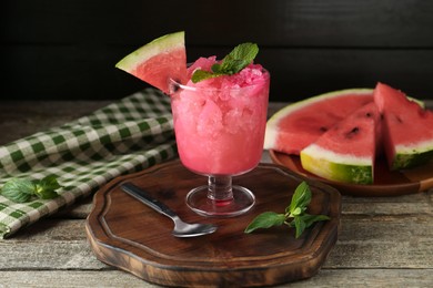 Photo of Tasty watermelon sorbet in glass dessert bowl, fresh fruit, mint and spoon on wooden table