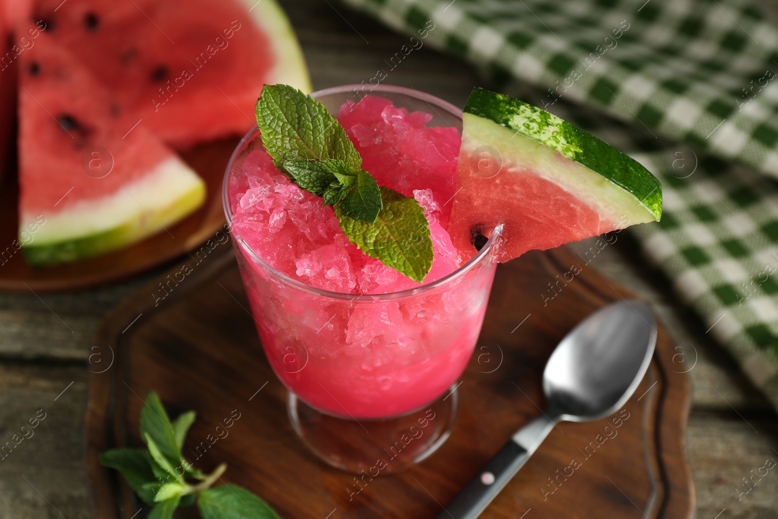 Photo of Tasty watermelon sorbet in glass dessert bowl, fresh fruit, mint and spoon on wooden table, closeup