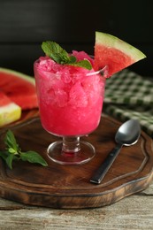 Photo of Tasty watermelon sorbet in glass dessert bowl, fresh fruit, mint and spoon on wooden table