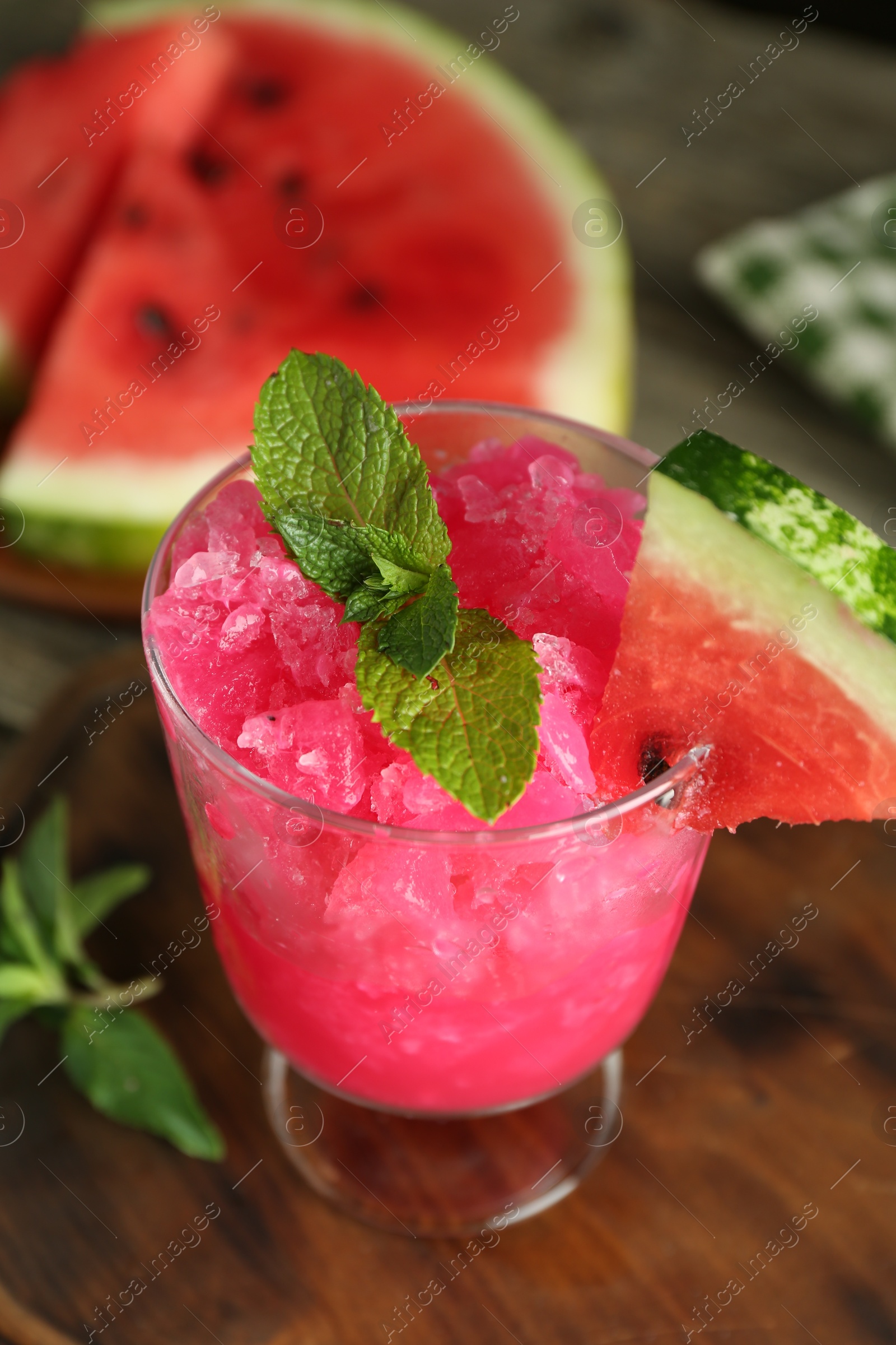 Photo of Tasty watermelon sorbet in glass dessert bowl, fresh fruit and mint on table, closeup