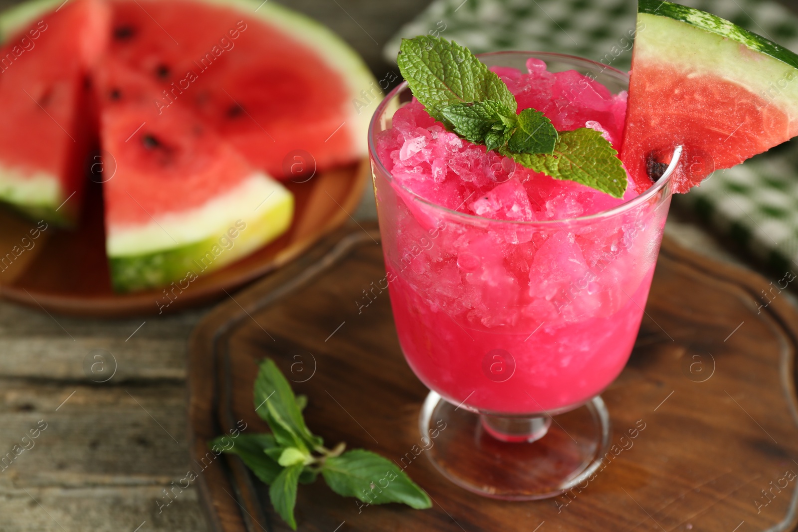 Photo of Tasty watermelon sorbet in glass dessert bowl, fresh fruit and mint on wooden table, closeup