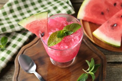 Photo of Tasty watermelon sorbet in glass dessert bowl, fresh fruit, mint and spoon on wooden table, closeup