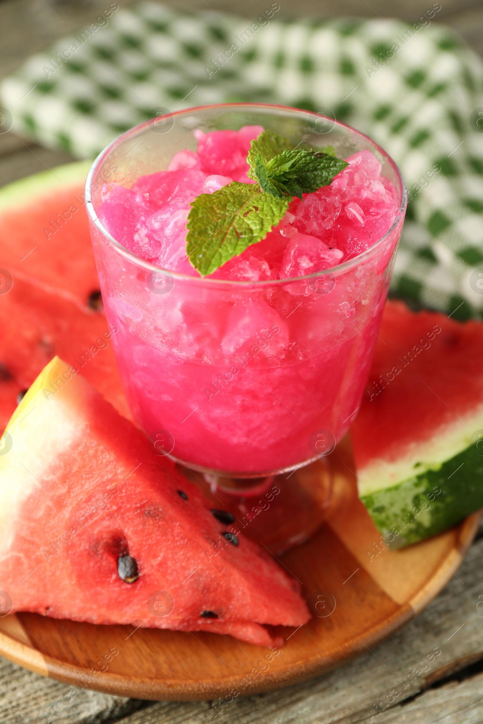 Photo of Tasty watermelon sorbet in glass dessert bowl, fresh fruit and mint on wooden table, closeup