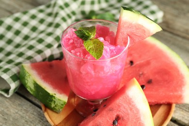 Photo of Tasty watermelon sorbet in glass dessert bowl, fresh fruit and mint on wooden table, closeup