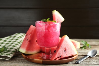 Photo of Tasty watermelon sorbet in glass dessert bowl, fresh fruit, mint and spoon on wooden table