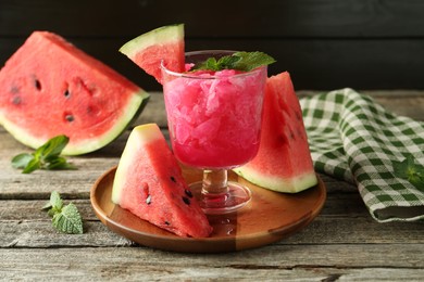 Photo of Tasty watermelon sorbet in glass dessert bowl, fresh fruit and mint on wooden table