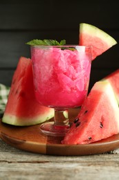 Photo of Tasty watermelon sorbet in glass dessert bowl, fresh fruit and mint on wooden table