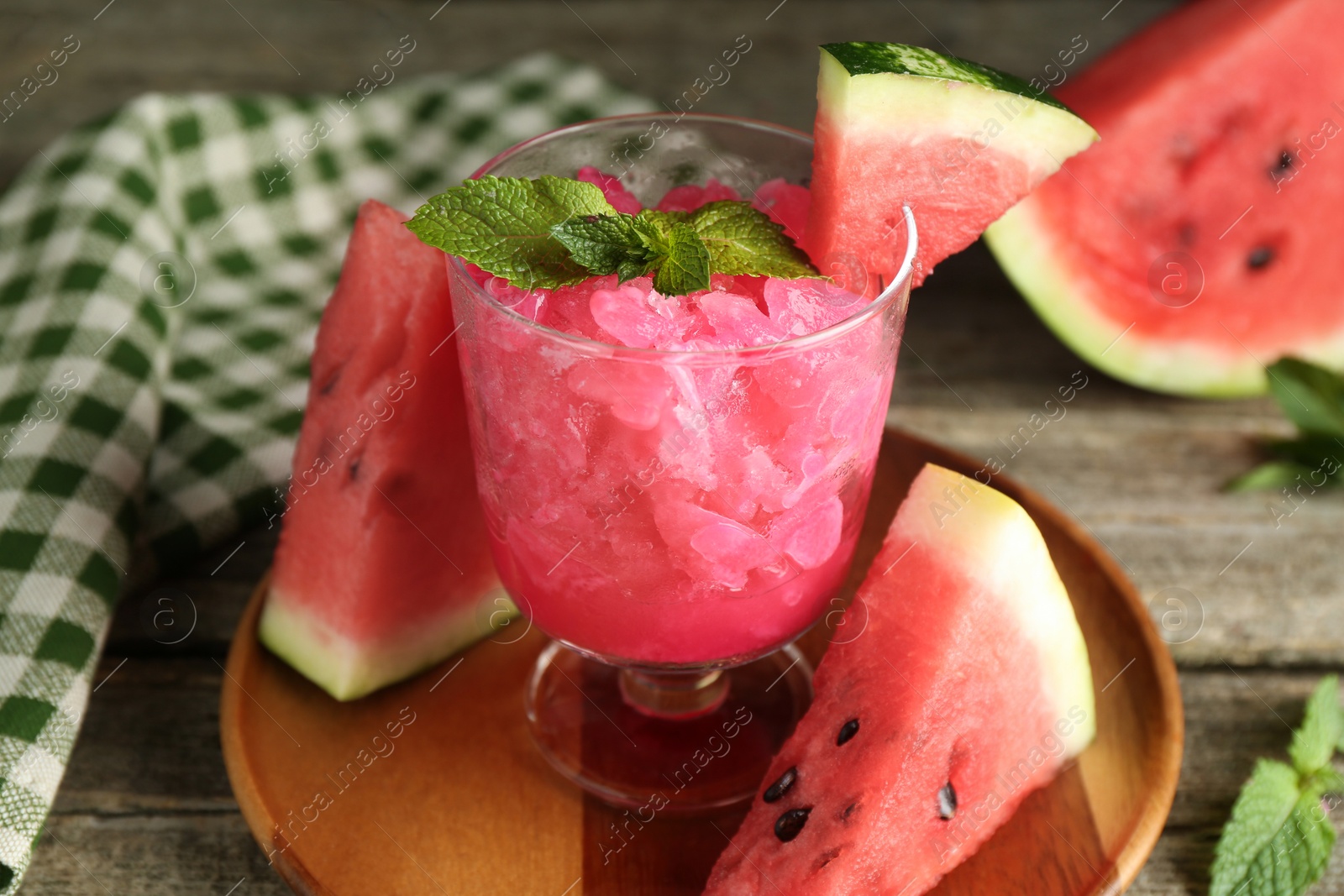 Photo of Tasty watermelon sorbet in glass dessert bowl, fresh fruit and mint on wooden table, closeup