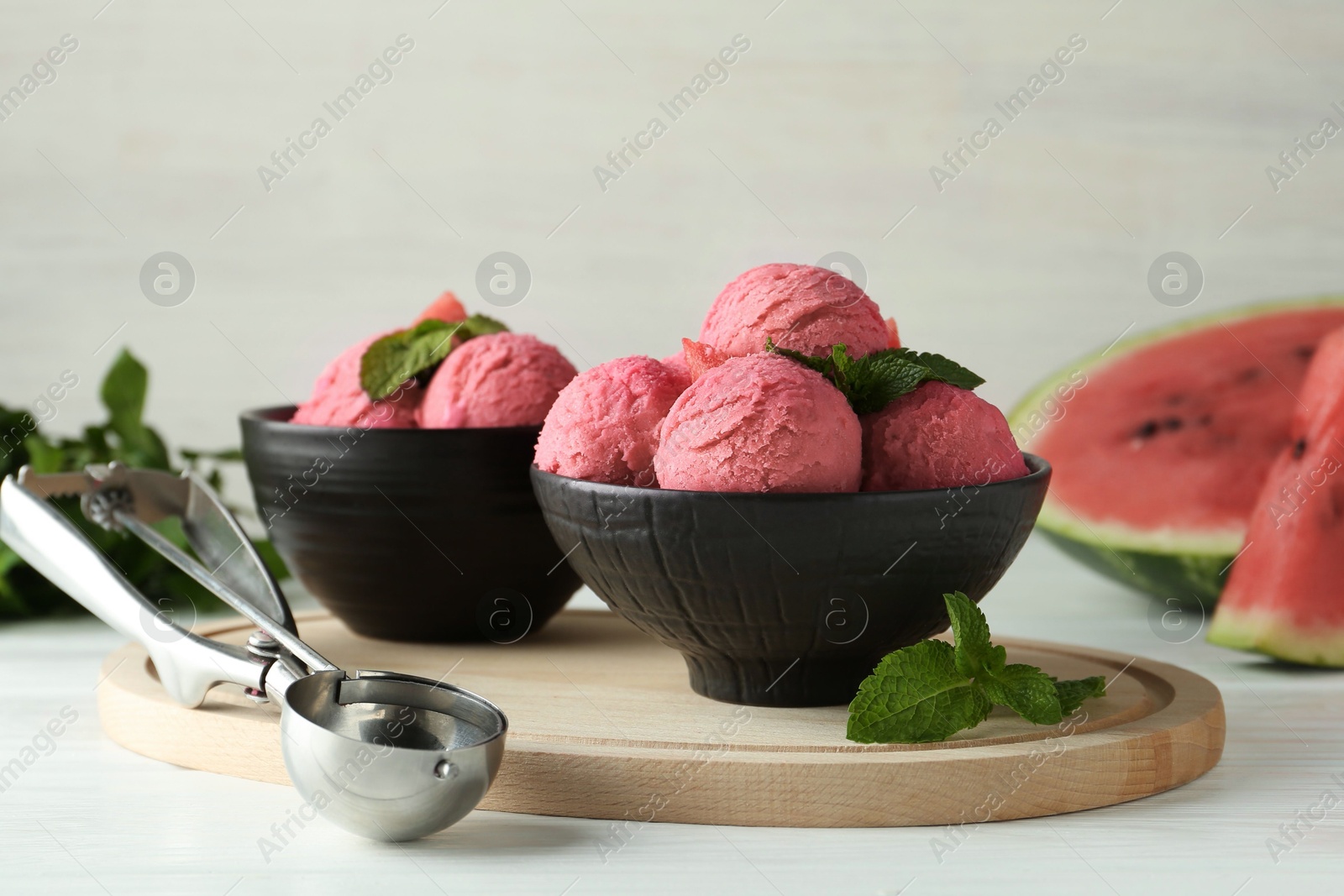 Photo of Scoops of tasty watermelon sorbet in bowls, fresh fruit and mint on white wooden table