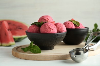 Photo of Scoops of tasty watermelon sorbet in bowls, fresh fruit and mint on white wooden table