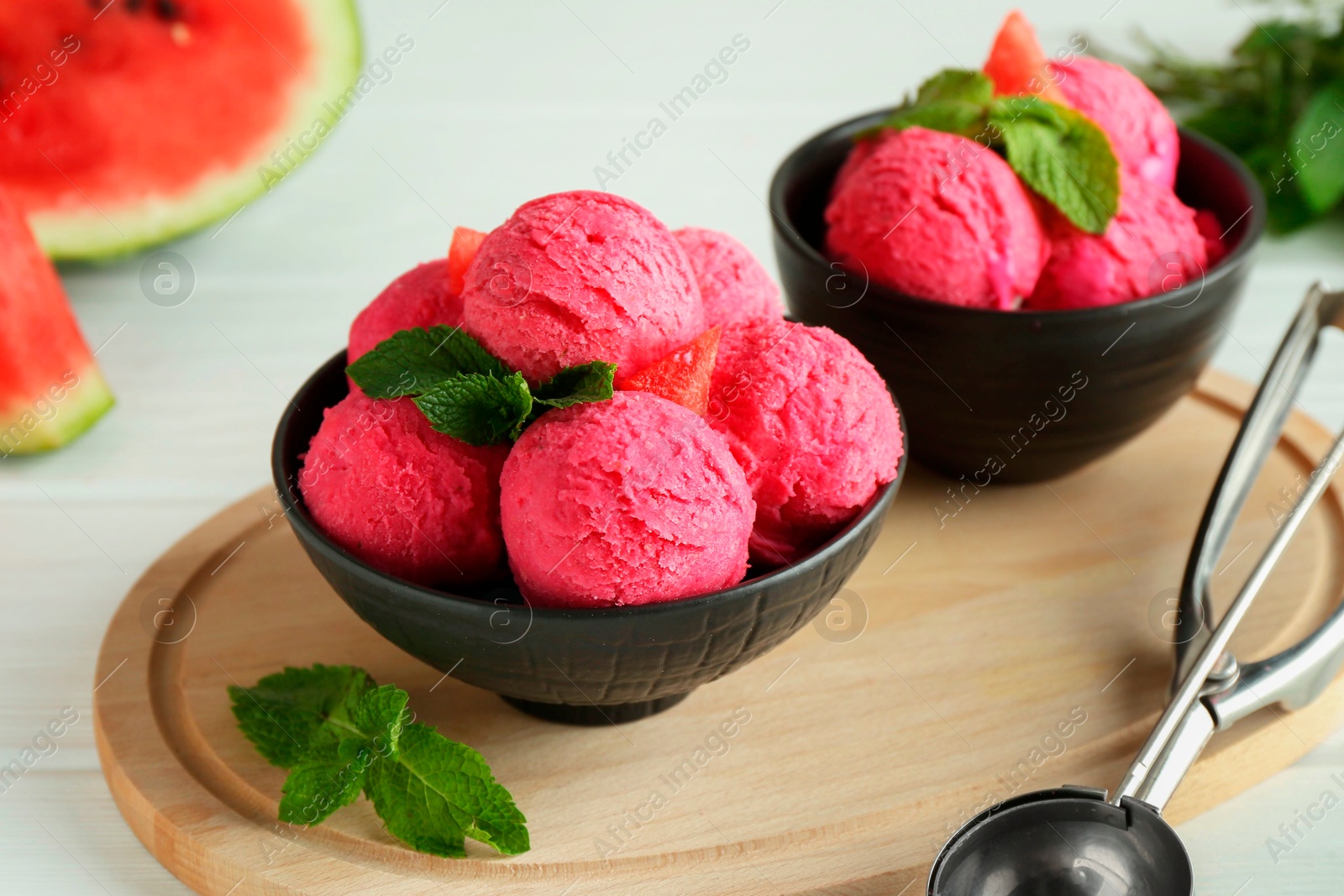 Photo of Scoops of tasty watermelon sorbet in bowls and mint on white table, closeup