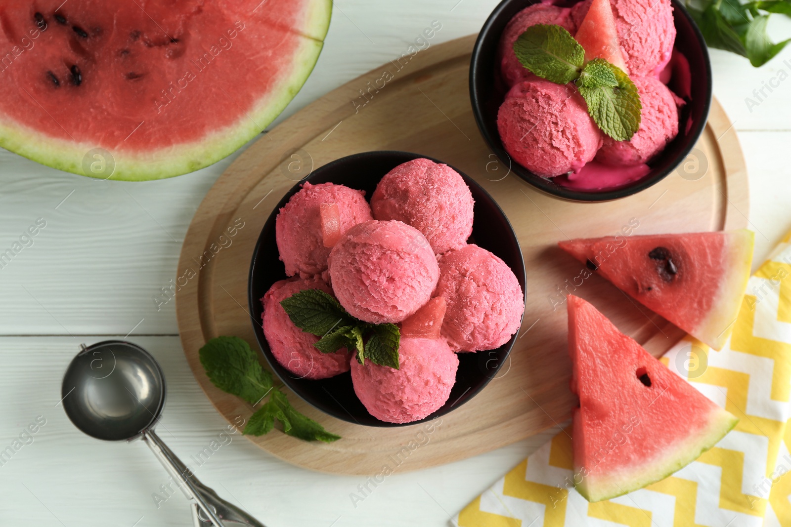 Photo of Scoops of tasty watermelon sorbet in bowls, fresh fruit and mint on white wooden table, top view