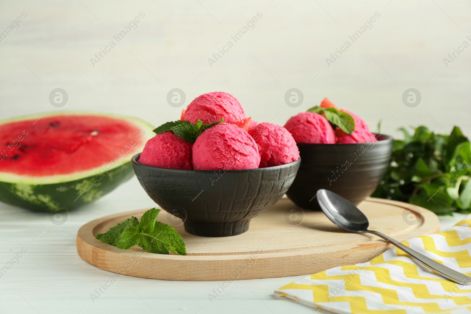 Photo of Scoops of tasty watermelon sorbet in bowls, fresh fruit, mint and spoon on white wooden table