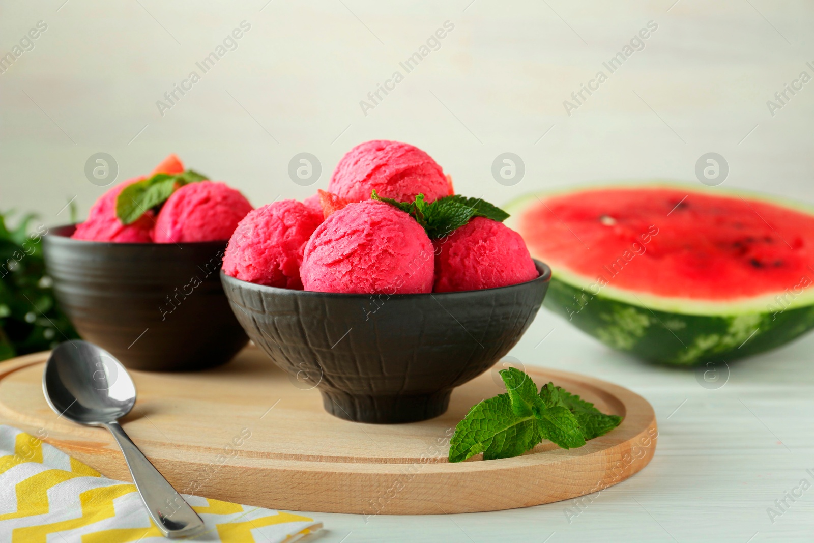 Photo of Scoops of tasty watermelon sorbet in bowls, fresh fruit, mint and spoon on white wooden table