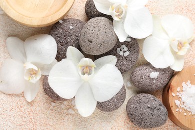 Photo of Spa stones, sea salt and beautiful orchid flowers on beige textured background, flat lay