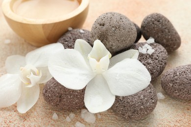 Spa stones, sea salt and beautiful orchid flowers on beige textured surface, closeup