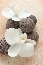 Photo of Spa stones and beautiful orchid flowers on beige textured background, closeup