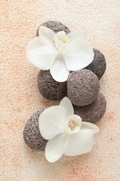 Photo of Spa stones and beautiful orchid flowers on beige textured background, flat lay