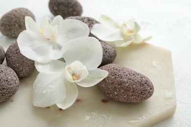 Photo of Spa stones and beautiful orchid flowers on white surface, closeup