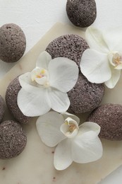 Spa stones and beautiful orchid flowers on white background, flat lay