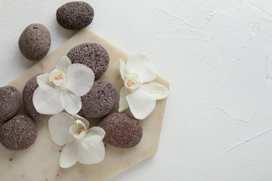 Photo of Spa stones and beautiful orchid flowers on white textured background, flat lay. Space for text