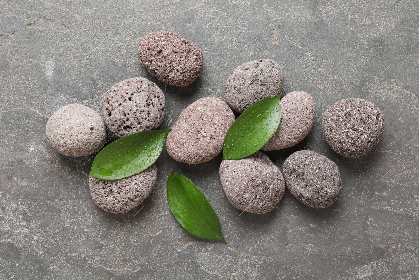 Photo of Wet spa stones and green leaves on grey textured background, flat lay