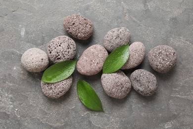 Wet spa stones and green leaves on grey textured background, flat lay