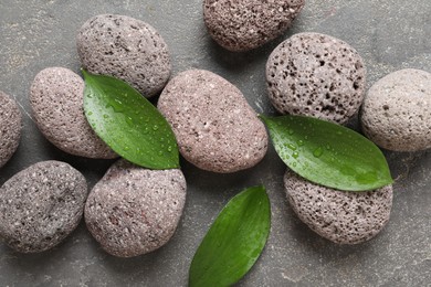 Wet spa stones and green leaves on grey textured background, flat lay