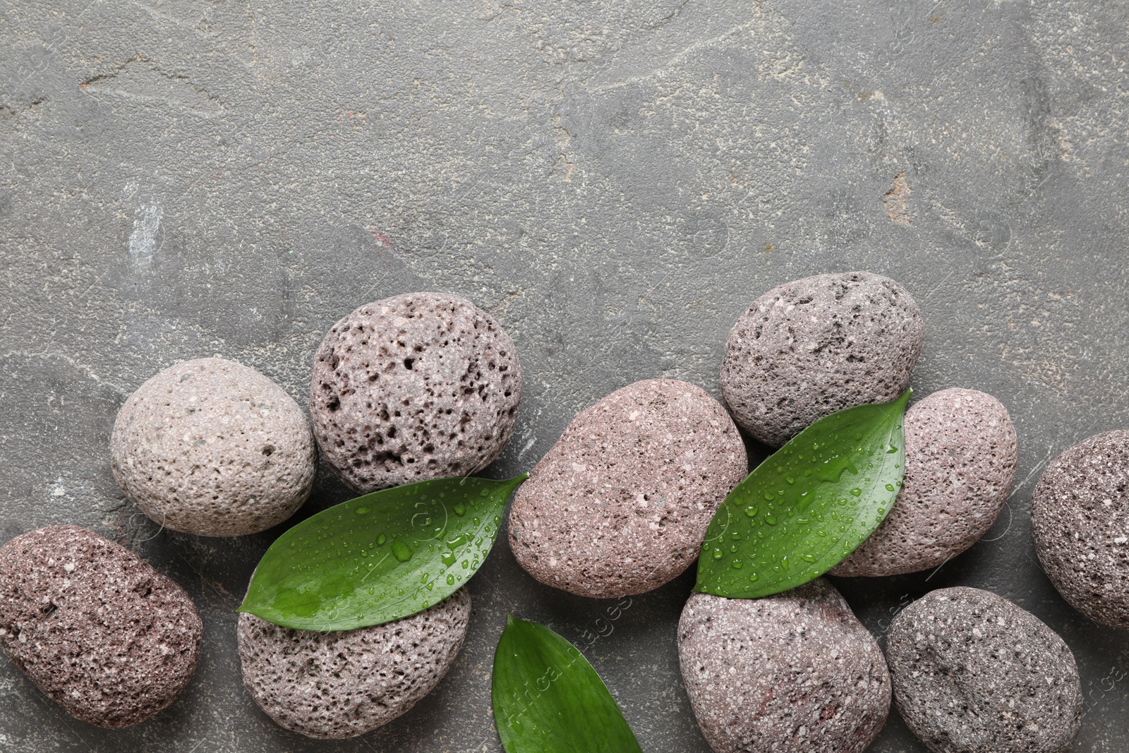 Photo of Wet spa stones and green leaves on grey textured background, flat lay. Space for text