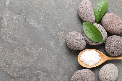 Wet spa stones, sea salt and green leaves on grey textured background, flat lay. Space for text