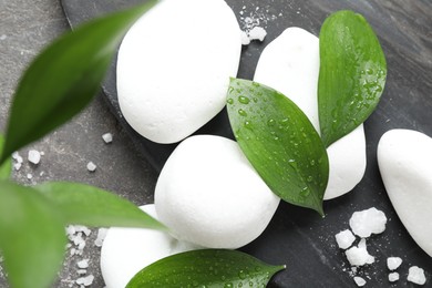 Wet spa stones, sea salt and green leaves on grey textured background, flat lay