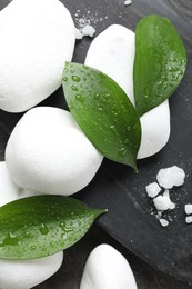 Photo of Wet spa stones, sea salt and green leaves on grey background, flat lay