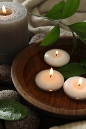 Photo of Burning candles and green leaves in water on table, closeup