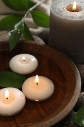 Photo of Burning candles and green leaves in water on table, closeup