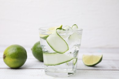 Refreshing water with sliced cucumber and lime in glass on white wooden table, closeup