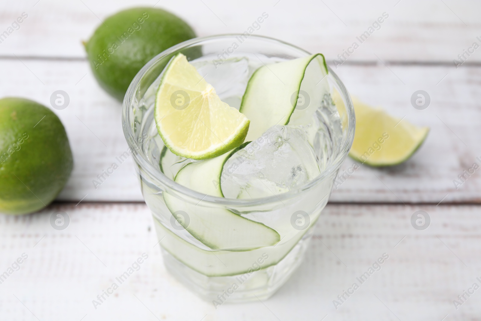 Photo of Refreshing water with sliced cucumber and lime in glass on white wooden table, closeup