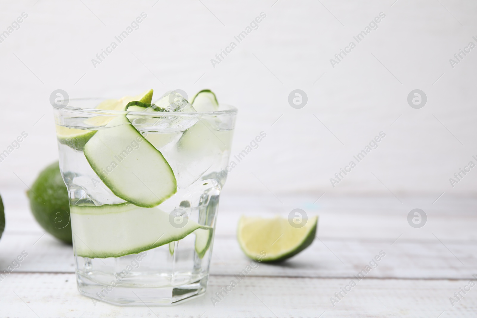 Photo of Refreshing water with sliced cucumber and lime in glass on white wooden table, closeup. Space for text