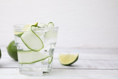 Refreshing water with sliced cucumber and lime in glass on white wooden table, closeup. Space for text