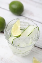 Photo of Refreshing water with sliced cucumber and lime in glass on white wooden table, closeup